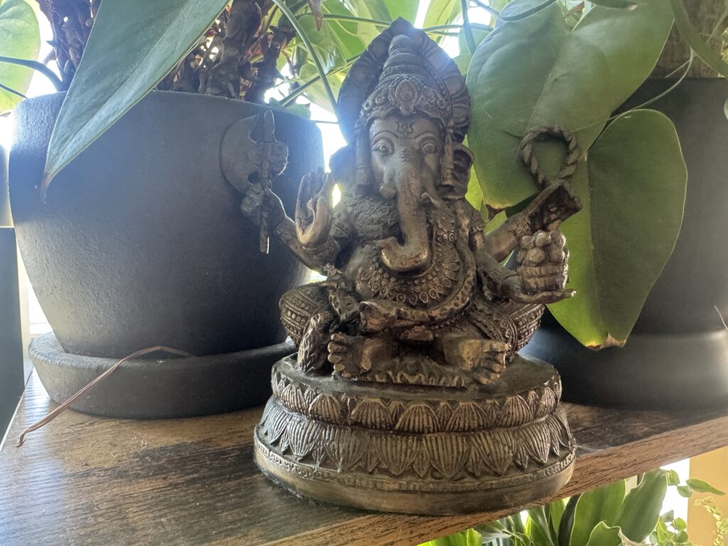 Ganapati statue on a wooden shelf among green plants, symbolizing new beginnings in mythic yoga practice
